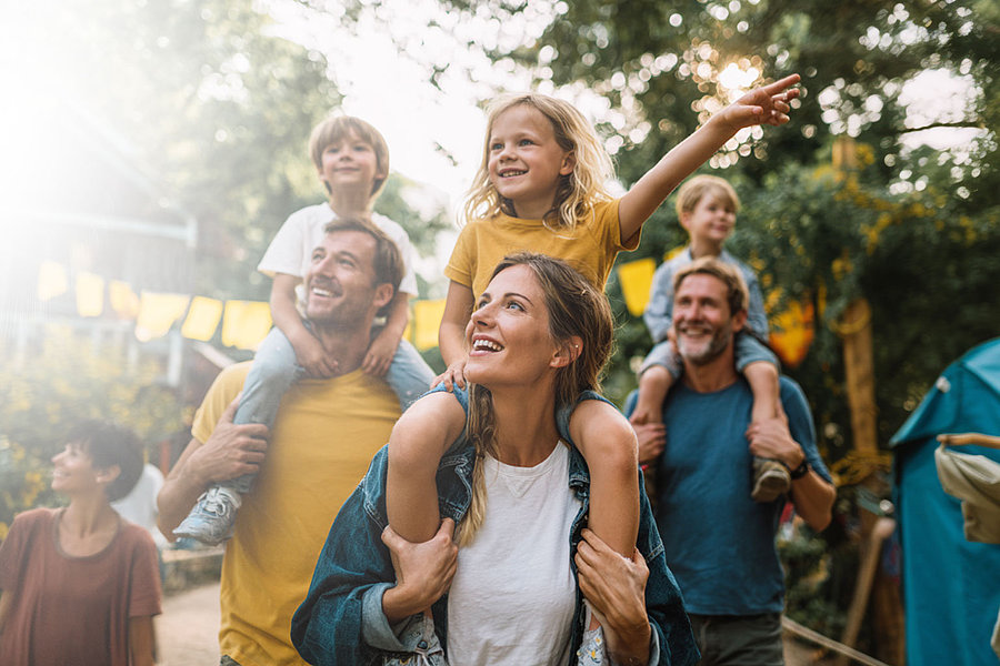 Mehrere Erwachsene tragen Kinder auf den Schultern. Sie gehen durch eine Siedlung.