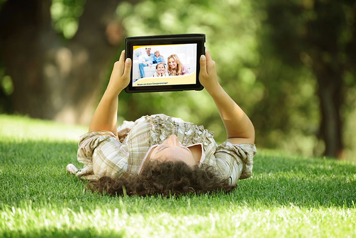 Eine Frau liegt im Gras und liest auf dem Tablet.