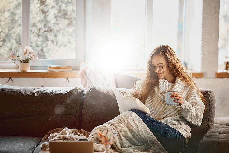 Eine Frau sitzt auf einer Couch und liest ein Buch.
