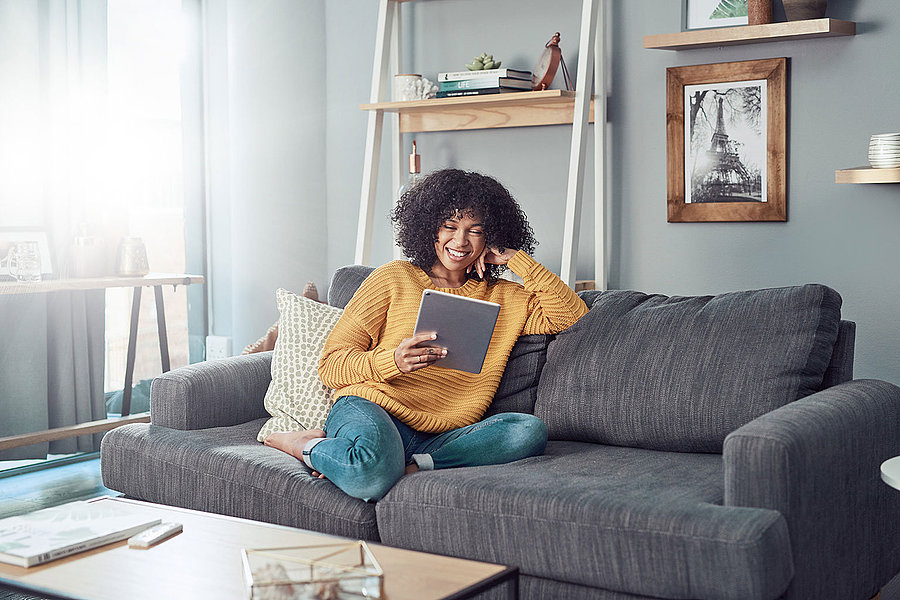 Eine Frau sitzt auf einer Couch und hält ein Tablet in der Hand.