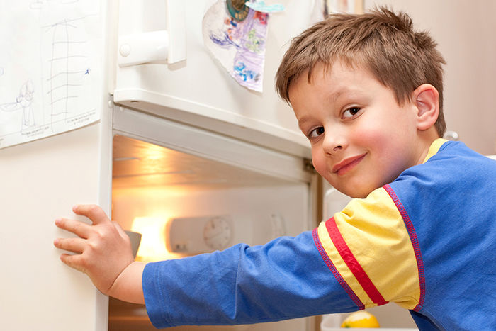 Ein Junge steht vor dem geöffneten Kühlschrank. Er schaut rückwärts über die linke Schulter.