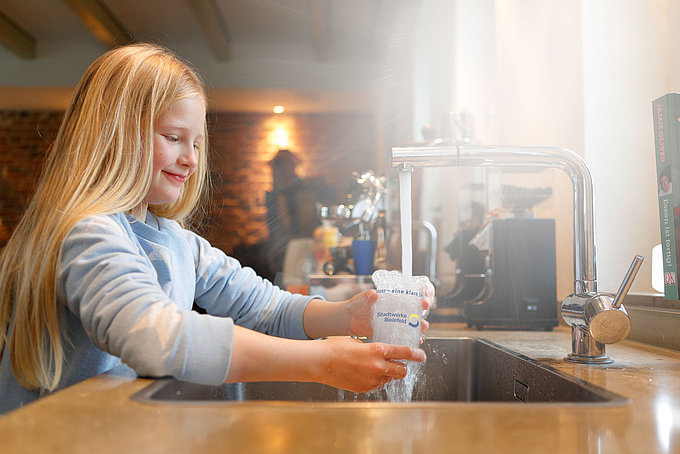Ein Mädchen füllt ein Glas Wasser am Wasserhahn auf.