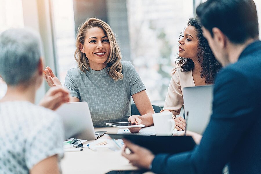 Drei Frauen und ein Mann sitzen an einem Tisch. Sie sind in einem Besprechungsraum Ihres Unternehmens.